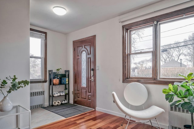 foyer with radiator heating unit, baseboards, and wood finished floors