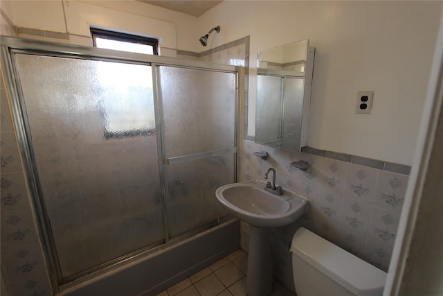 full bath with tile patterned flooring, toilet, a sink, tile walls, and combined bath / shower with glass door