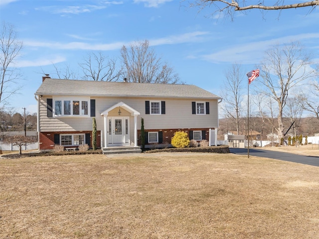 bi-level home featuring brick siding, a front lawn, and a chimney