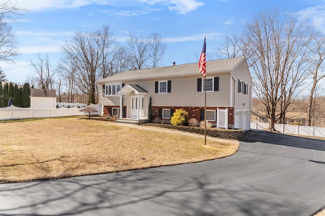 split foyer home featuring driveway, a garage, fence, and brick siding