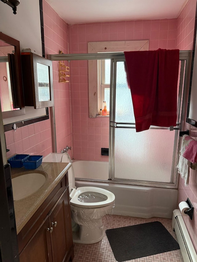 full bath with tile walls, bath / shower combo with glass door, a baseboard heating unit, vanity, and tile patterned floors