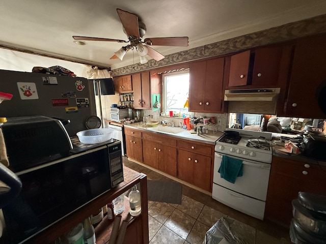 kitchen with white gas stove, light countertops, freestanding refrigerator, a sink, and under cabinet range hood