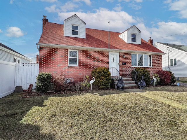 cape cod house featuring brick siding, a chimney, a front lawn, and fence