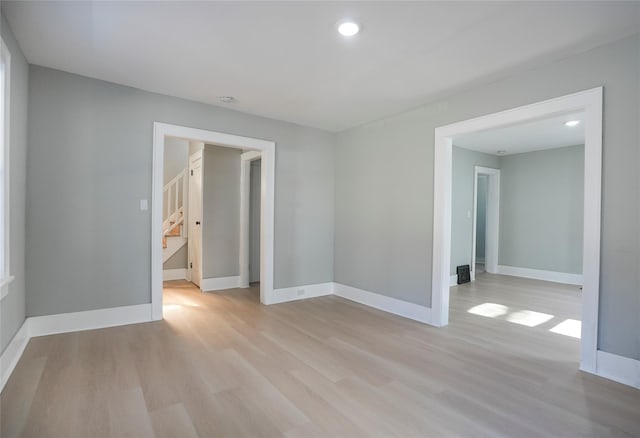 empty room featuring recessed lighting, baseboards, light wood finished floors, and stairs