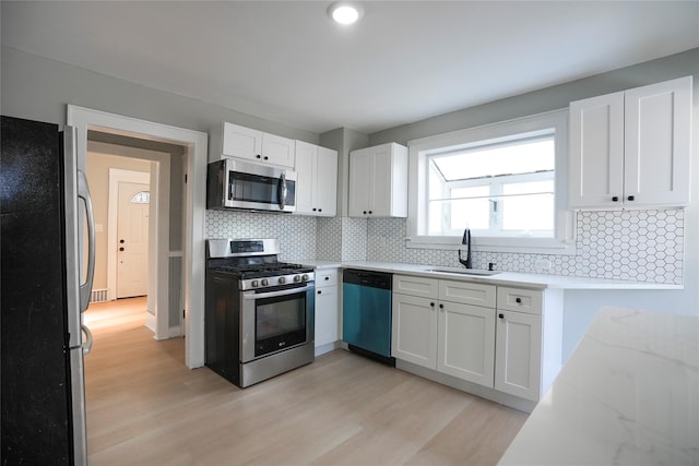 kitchen featuring appliances with stainless steel finishes, light wood-style floors, white cabinets, a sink, and light stone countertops