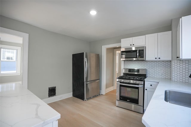 kitchen with light wood finished floors, visible vents, appliances with stainless steel finishes, light stone countertops, and backsplash