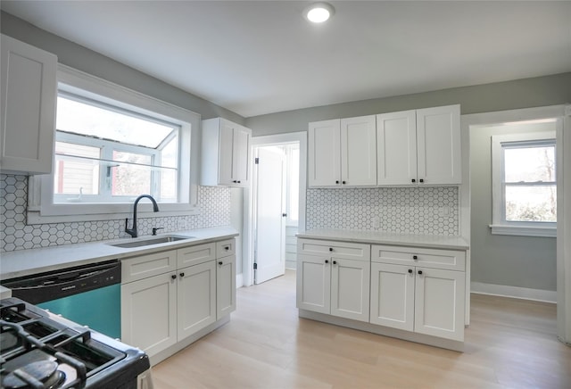 kitchen featuring dishwashing machine, a sink, white cabinets, light countertops, and light wood-type flooring