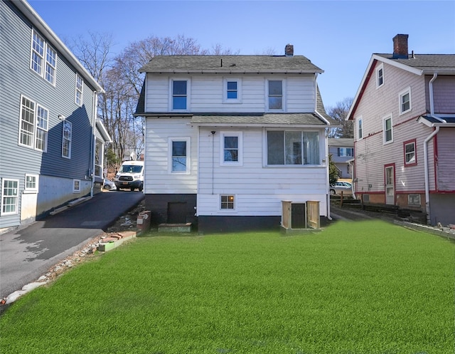 back of property with driveway, a lawn, a chimney, and roof with shingles