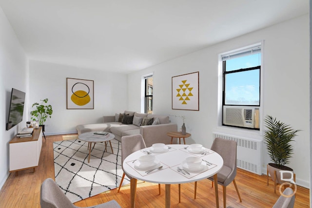 dining area with radiator, baseboards, cooling unit, and light wood-type flooring