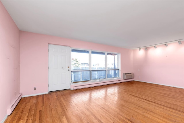 empty room with a baseboard heating unit, baseboards, light wood finished floors, and a wall mounted AC