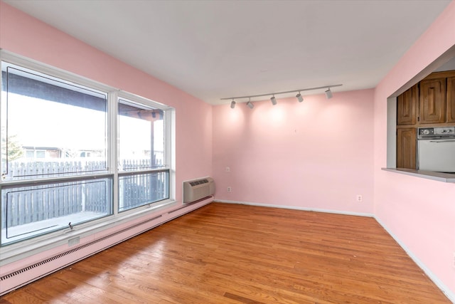 empty room featuring light wood finished floors, baseboards, a baseboard heating unit, and an AC wall unit