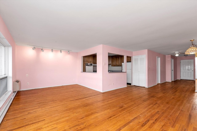 unfurnished living room with a baseboard heating unit, track lighting, baseboards, and wood finished floors