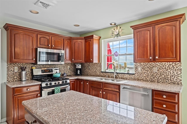 kitchen with stainless steel appliances, visible vents, decorative backsplash, a sink, and light stone countertops