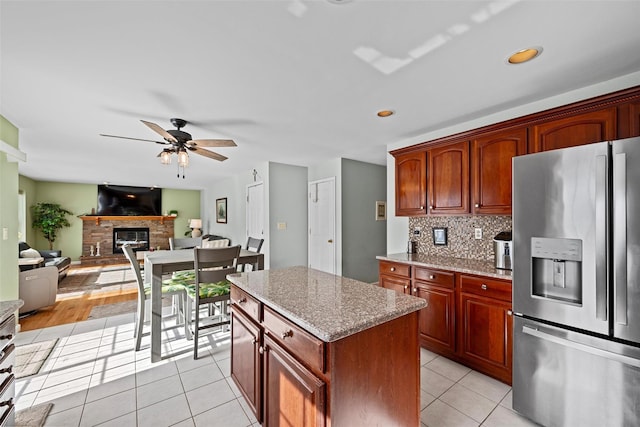 kitchen with light tile patterned floors, a stone fireplace, a kitchen island, open floor plan, and stainless steel fridge