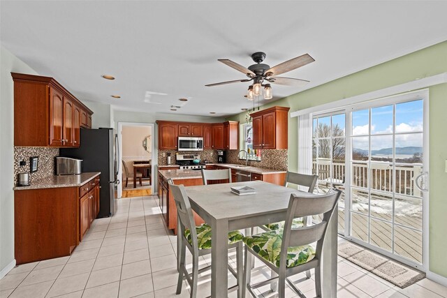 kitchen featuring light tile patterned floors, decorative backsplash, appliances with stainless steel finishes, a sink, and ceiling fan