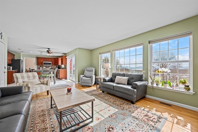 living room featuring ceiling fan, light wood-style flooring, visible vents, and baseboards