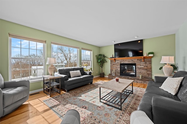 living area with light wood-style floors, visible vents, baseboards, and a stone fireplace