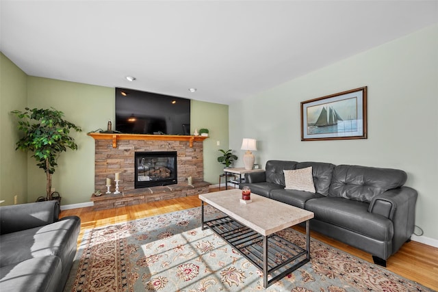 living room with baseboards, wood finished floors, and a stone fireplace