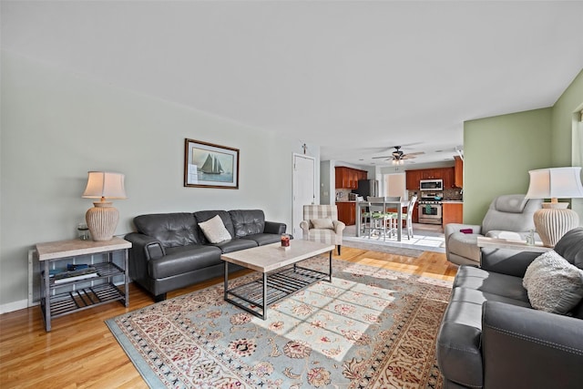 living room with light wood-style flooring, baseboards, and ceiling fan