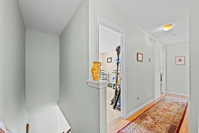 hallway featuring baseboards, visible vents, and wood finished floors