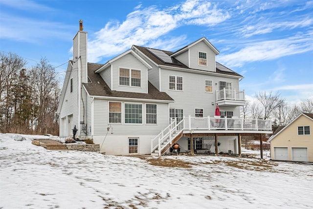 snow covered house featuring a detached garage, a chimney, stairway, a balcony, and a deck