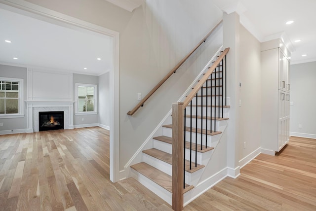 stairway featuring a warm lit fireplace, baseboards, crown molding, and wood finished floors