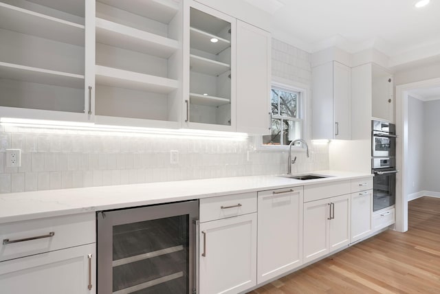 kitchen with tasteful backsplash, white cabinets, wine cooler, stainless steel double oven, and a sink