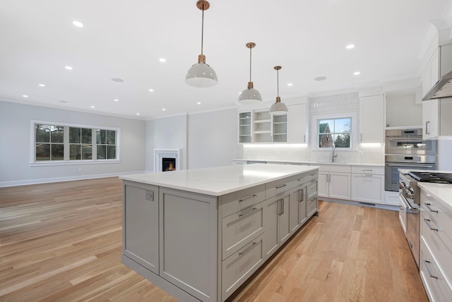 kitchen featuring gray cabinetry, a lit fireplace, backsplash, a center island, and crown molding