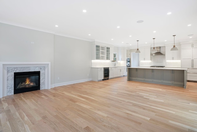 kitchen featuring beverage cooler, wall chimney exhaust hood, ornamental molding, white cabinetry, and backsplash