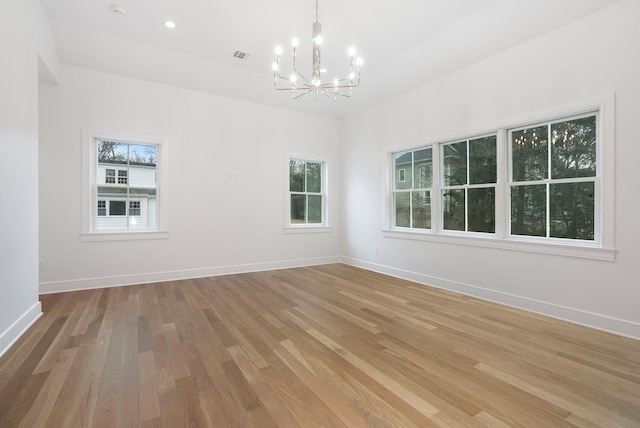 empty room with an inviting chandelier, light wood-style flooring, visible vents, and baseboards