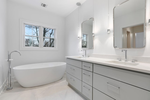 bathroom with double vanity, a freestanding tub, a sink, and visible vents