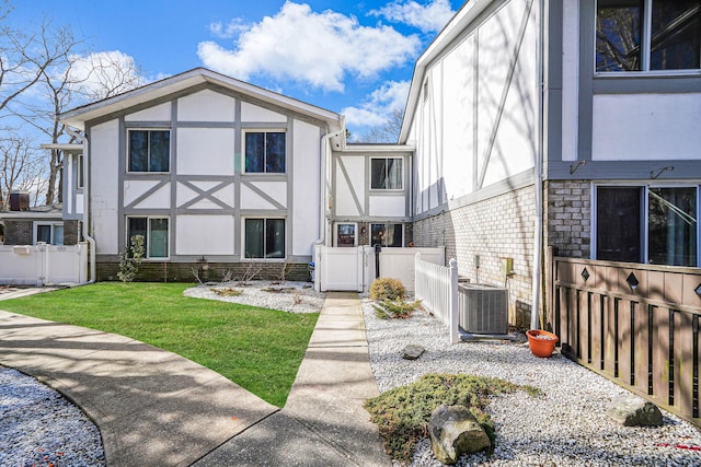 view of front facade with cooling unit, brick siding, fence, stucco siding, and a front lawn