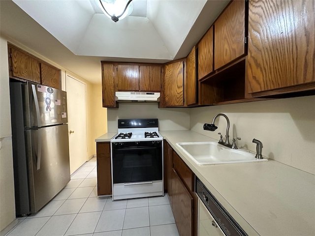 kitchen with under cabinet range hood, a sink, range with gas stovetop, light countertops, and freestanding refrigerator