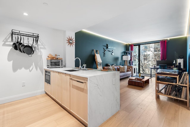 kitchen featuring light countertops, light wood-style flooring, open floor plan, light brown cabinets, and a sink