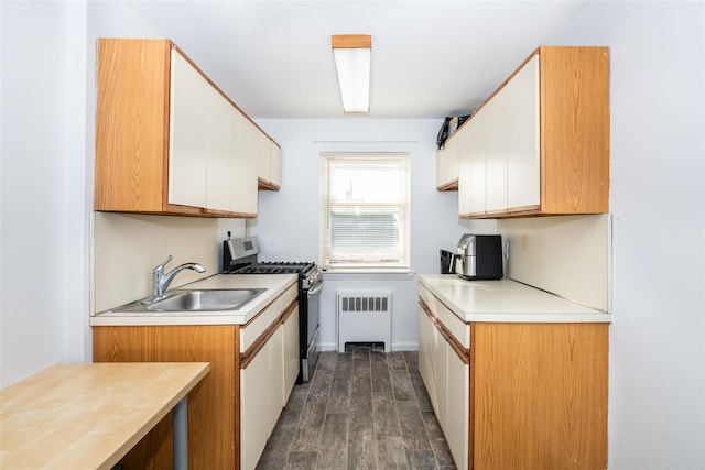 kitchen featuring light countertops, radiator heating unit, white cabinetry, a sink, and stainless steel gas range