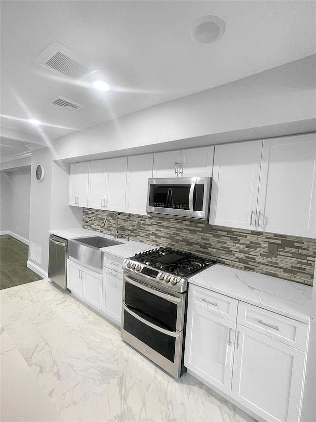 kitchen featuring stainless steel appliances, light stone countertops, white cabinets, backsplash, and sink