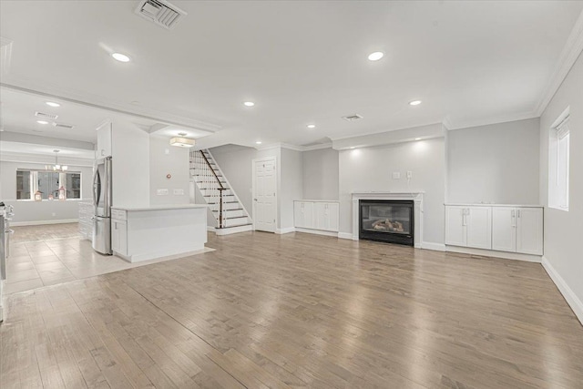 unfurnished living room with a glass covered fireplace, visible vents, crown molding, and stairs