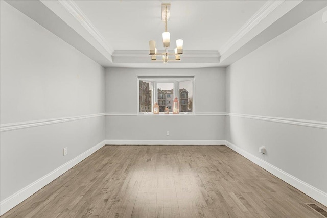 unfurnished dining area with ornamental molding, a raised ceiling, a notable chandelier, and wood finished floors