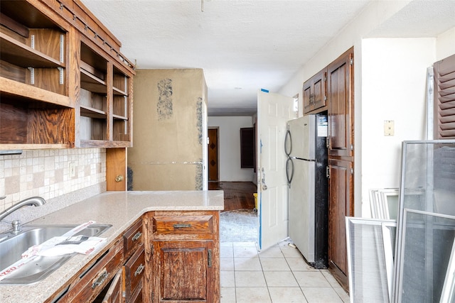 kitchen featuring stainless steel refrigerator, sink, tasteful backsplash, light tile patterned floors, and a textured ceiling