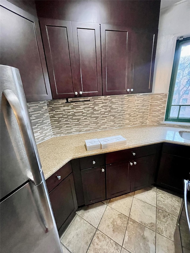 kitchen with decorative backsplash, dark brown cabinetry, and stainless steel refrigerator