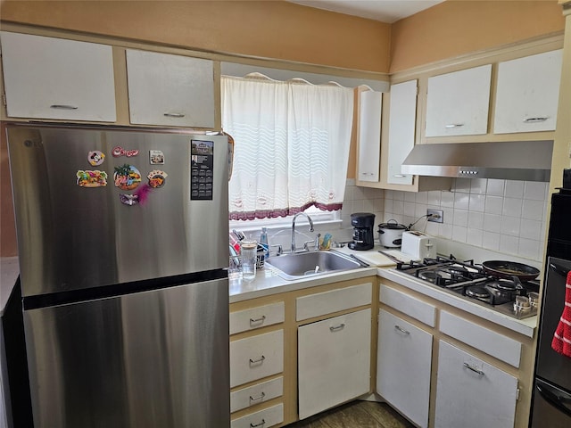 kitchen with under cabinet range hood, white gas stovetop, a sink, light countertops, and freestanding refrigerator