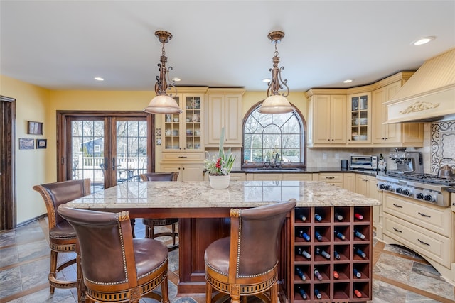 kitchen featuring french doors, stainless steel gas cooktop, decorative backsplash, cream cabinets, and premium range hood