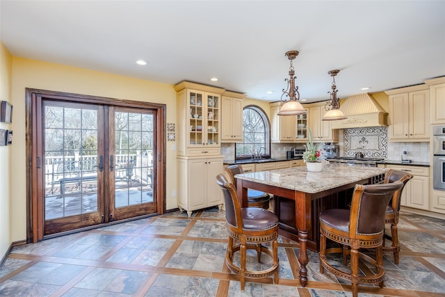 kitchen featuring a sink, custom range hood, backsplash, and cream cabinetry