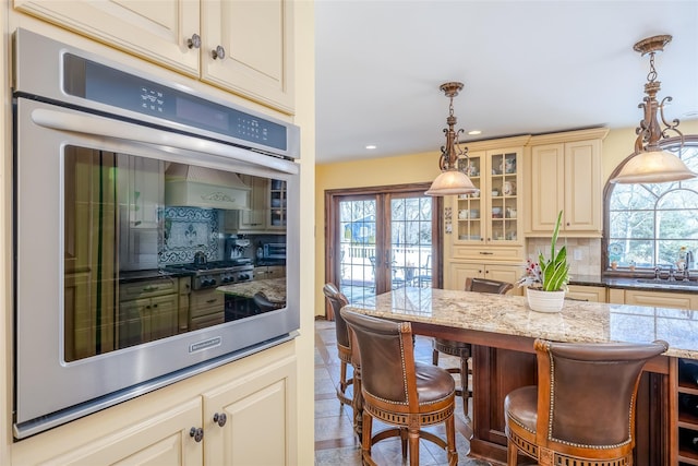 kitchen featuring tasteful backsplash, cream cabinets, double oven, a sink, and a kitchen breakfast bar