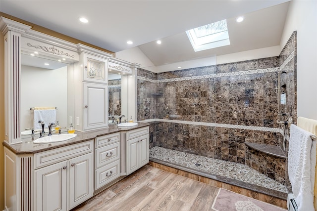 full bathroom with a tile shower, vaulted ceiling with skylight, wood finished floors, and a sink