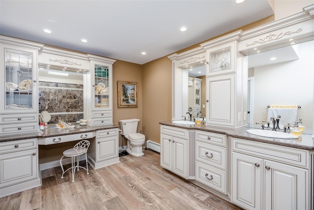 full bath with double vanity, wood finished floors, baseboard heating, and a sink