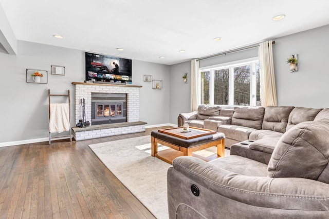 living room with recessed lighting, dark wood-style flooring, a brick fireplace, and baseboards