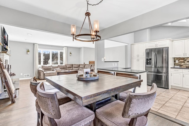 dining area with visible vents, a fireplace with raised hearth, light wood-style floors, vaulted ceiling, and a chandelier