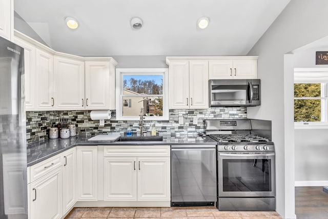 kitchen with dark countertops, appliances with stainless steel finishes, a sink, and lofted ceiling