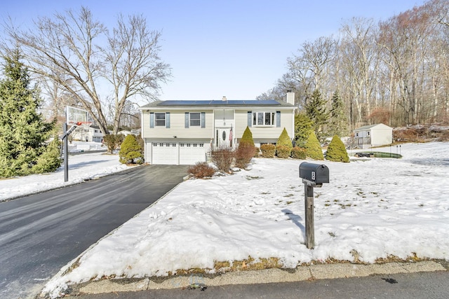 split foyer home featuring aphalt driveway, a chimney, and an attached garage